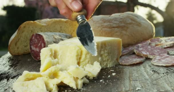 木製のまな板の上にパルメザンチーズの組成物 片手でナイフを取り 品質を味わうためにいくつかの作品を破る コンセプト イタリア チーズ — ストック動画