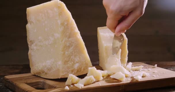 木製のまな板の上にパルメザンチーズの組成物 片手でナイフを取り 品質を味わうためにいくつかの作品を破る コンセプト イタリア チーズ — ストック動画