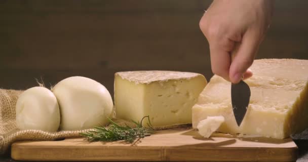 木製のまな板にイタリアチーズの構成 片手でナイフを取り 品質を味わうためにいくつかの作品を破る コンセプト イタリア チーズ — ストック動画