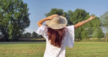 Beyaz yazlık elbise ve şapka doğa, çayırda çalışan günde zevk içinde kadın ağır çekim video, arka görünüm 