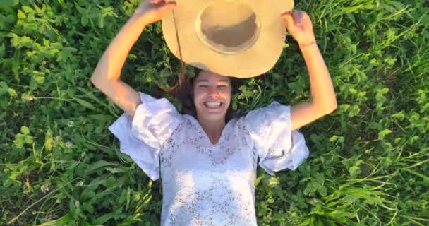 慢动作视频 笑女人在白色夏装躺在绿色的草地上 覆盖着脸与头 顶视图 — 图库视频影像