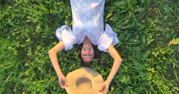 妇女在白色夏天礼服的慢动作视频躺在绿色的草草甸和覆盖的面孔与头 顶视图 — 图库视频影像