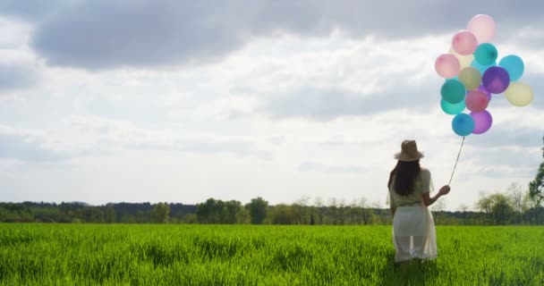 カラフルな風船を押し 緑の草の芝生に立っている女性のスロー モーション ビデオ 背面図 — ストック動画