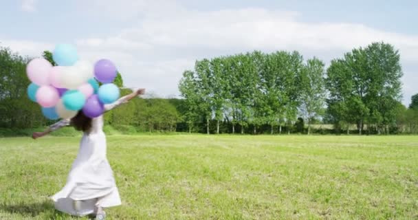 風船を押しと実行して 緑の草の牧草地で回転するドレスを着た女性のスロー モーション ビデオ — ストック動画