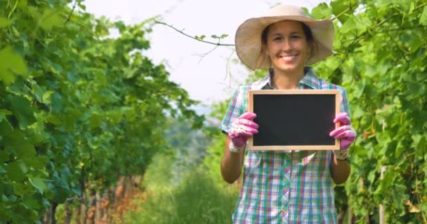 葡萄畑のプランテーションと示す黒板で立っている農夫女性を笑顔のビデオ — ストック動画