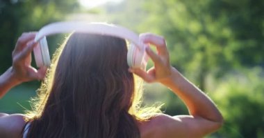 Arkadan görünüm, ağır çekim video kadın dinleme müzik kulaklık ve rahatlatıcı yaz orman ağaçları ile 