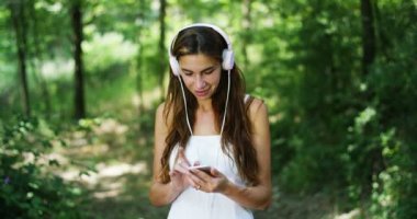 mutlu kadın kulaklık müzik dinleme gülümseyen ve yaz orman ağaçları ile dans ve cep telefonuyla video 