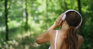 ağır çekim video kadın dinleme müzik kulaklık ve rahatlatıcı yaz orman ağaçlarıyla, arkadan görünüm