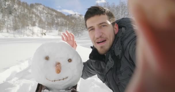 Hóember mellett álló ember és videohívás a hegyek ellen