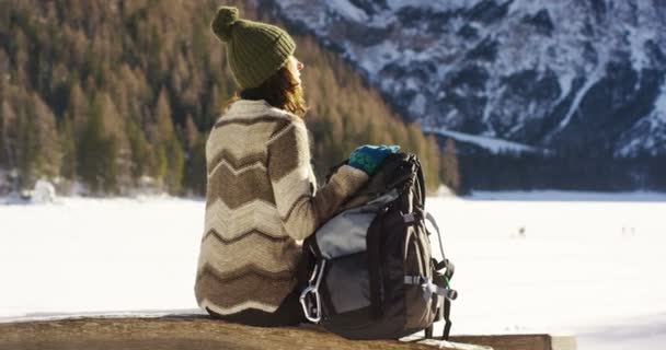 女の子は かかっているし 彼の腕の中で雪の中歩くハイキング バックパックを保持している彼の前に雪の山を見てリラックスします コンセプト リラクゼーション ハイキング — ストック動画