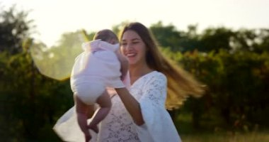 Anne ve küçük kız mutlu oynamak doğada, Anne kucağında bebeği alır ve rahatla, 4 k uhd bir güneş bir aile olarak birlikte olmak mutlu