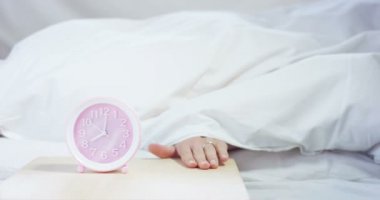 Güzel bir genç kız sıcak bir yatakta zayıf up için çalar saat kapalı geçiş için basit bir çalışma günü kaplı bir yumuşak sıcak beyaz battaniye, beyaz bir arka plan üzerinde ile.