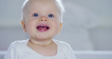 Bir bebek, büyük mavi gözleri ve açık renk saçlı, bir çocuk oturur ve bembeyaz bir battaniye var gülümsüyor, beyaz zemin üzerine annesi bakar. Konsept: çocuk, çocuk, Bebek, bebekler, yeni nesil.