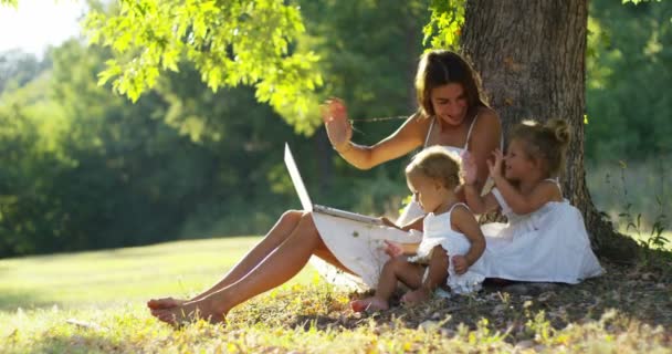 在晴朗的一天我的母亲给她的女儿读了一本书在一棵树下 放松一下母亲和女儿 在讲故事的时间之间的时刻 母亲和女儿的概念 — 图库视频影像