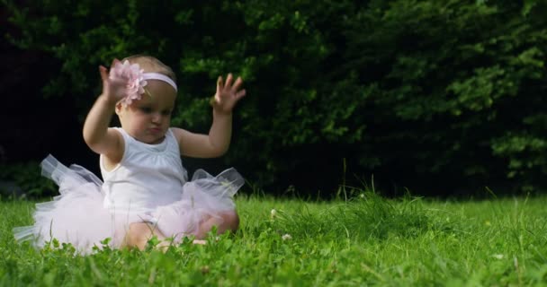 在一个阳光明媚的春日小女孩穿得像在花园周围旋转的芭蕾舞演员自己和微笑快乐 — 图库视频影像