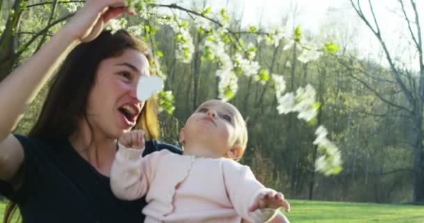 母親が赤ちゃんを彼女の腕にかかるし リラックス Uhd でサンシャインに家族の一員として一緒に幸せなママと小さな女の子が自然に楽しそうに遊んで — ストック動画