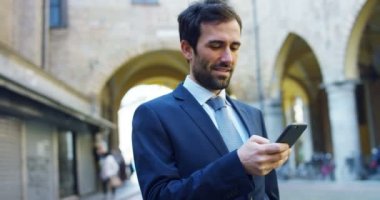 Telefonlara bir işadamı göndermek mesajları ve güzel iş Haberler için gülümsüyor ve arka planda bir kişi görmek. Konsept: teknoloji, telefon, iş gezileri, iş, wall street