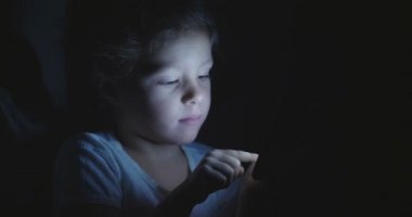 Çocuk akşam veya gece akşam ışığı, e-öğrenme, öğrenme ve basit teknolojileri kavramı ile tablet veya telefon kullanır. Çocuk ve uygulanan teknolojiler futuristik konsepti.