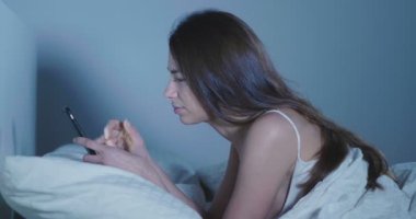 esmer kadın yatakta yatan ve smartphone tarama video