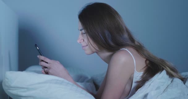Βίντεο Μελαχρινή Γυναίκα Ξαπλωμένη Στο Κρεβάτι Και Κοιτάζοντας Βιαστικά Smartphone — Αρχείο Βίντεο