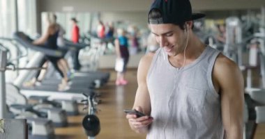Bir egzersiz ve diğer arasında istirahat ederken bir spor salonunda bir adam portresi telefonunu sosyal ağlar izlemek veya iletileri göndermek için kullanır. Kavramı: spor, kişisel antrenör, iletileri, telefon