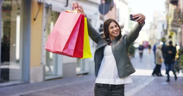 カラフルなショッピング バッグを押しながら携帯電話に Selfie 写真を撮る買い物客の女性のビデオ — ストック動画