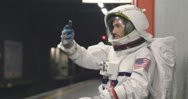 宇宙飛行士の服を着た男は スマート フォンを使用して呼び出し メッセージを送信します 彼の手で携帯電話を見ながら宇宙飛行士の笑顔 プロモーション メッセージと空間の呼び出し電話 — ストック動画
