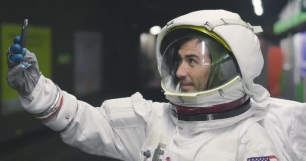 宇宙飛行士の服を着た男は スマート フォンを使用して呼び出し メッセージを送信します 彼の手で携帯電話を見ながら宇宙飛行士の笑顔 プロモーション メッセージと空間の呼び出し電話 — ストック動画
