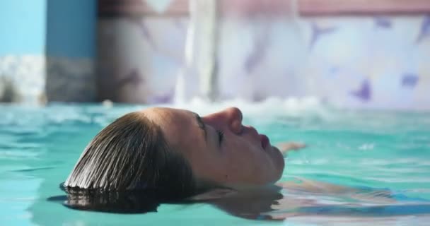美丽的年轻女孩 放松在水力按摩浴缸 在蓝色游泳衣 在蓝色的背景 水疗程序 身体按摩 水疗霜 水疗水疗 游泳池 — 图库视频影像