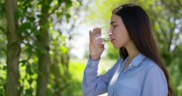 漂亮的年轻女孩拿着一杯 喝自然干净的水 在大自然的背景中 生态学 天然纯净来源 令人耳目一新 健康的环境 — 图库视频影像