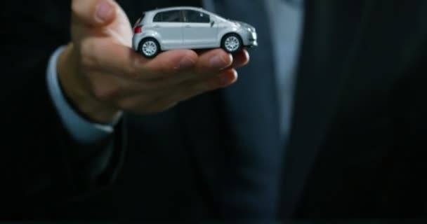 スーツとネクタイ姿の男性は 小さな自動車を示しています コンセプト 自動車保険 リース 購入新車 中古車や公共ガレージ — ストック動画