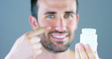 Çok yakışıklı bir adam gülümsüyor ve anti-kırışıklık ve anti-aging vücut bakımı için yüz kremi ve göz kontur koyar ve güzellik bilir. Konsept: Güzellik, krem, güzellik