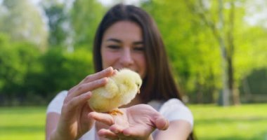 Güneşli bir günde, bir küçük sarı tutan genç güzel kız gülümseyerek tavuk ellerini, yeşil çim ve ağaçların, arka planda kavramı: çevre, aşk, ekoloji, genç kız, güzel doğası.