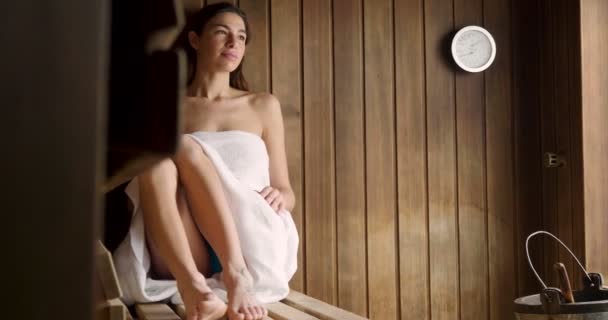 Eine schöne Frau mit einem weißen Handtuch geht in die Sauna: Die Sauna besteht aus Holz mit einem großen Fenster mit Blick auf den Schnee. Konzept von: Entspannung, Urlaub, Wellness-Center.