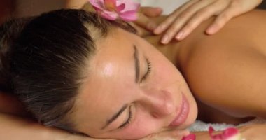 Spa salonu, romantik bir ortam, kulağının arkasında bir pembe çiçek bir sırt masajı yapıyor güzel bir genç kız (kadın). Konsept: spa prosedürler, vücut masajları, spa kremler, sakin ol, spa su tedavileri.