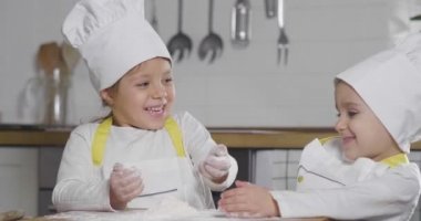 Mutfakta iki küçük kız aile için bir tatlı hazırlıyor. Yemek yapmayı öğrenirken unla oynamaya ve birbirlerine gülümsemeye başlarlar. Aşçılık dersleri, aile, eğitim kavramı.