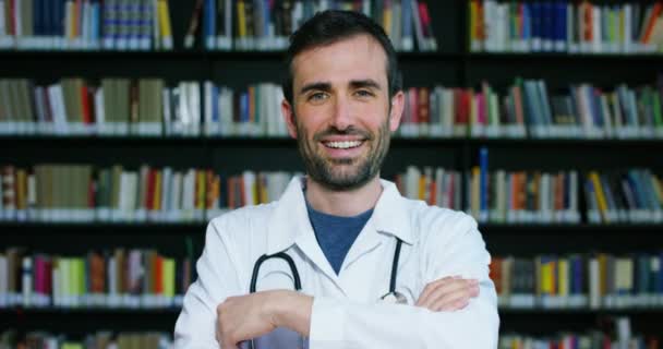 Médico Joven Hermoso Una Biblioteca Sonriendo Feliz Sosteniendo Libros Después — Vídeos de Stock