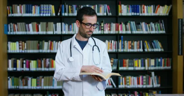 Médico Joven Hermoso Una Biblioteca Sonriendo Feliz Sosteniendo Libros Después — Vídeos de Stock