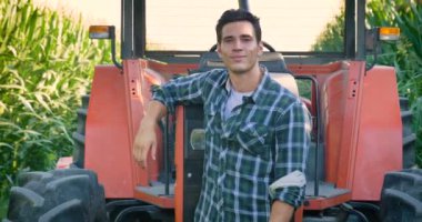 Alanında başarılı bir traktör ile çalışma güzel genç bir çiftçi (öğrenci) portresi gülümseyen, mutlu bir gömlek, Mısır alan. Kavram ekoloji, taşıma, çiftçiler, temiz hava, yiyecek, bio ürün