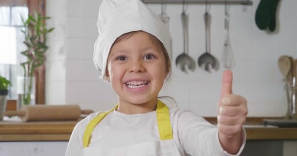 厨房里一个小女孩的肖像 打扮成一个专业的厨师 用她的手做确定 作为适当营养和正宗食物的标志 烹饪学校 — 图库视频影像