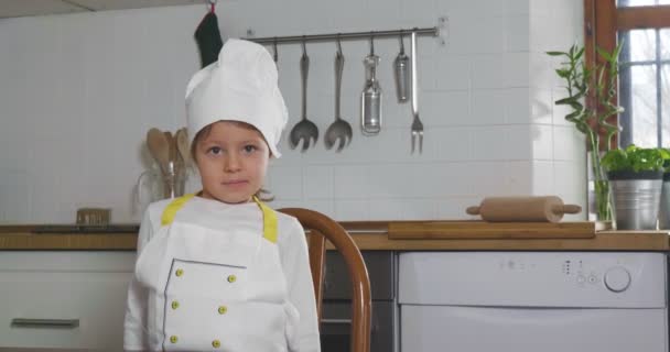適切な栄養と本物食品の印として彼女の手で を作るプロ料理人として服を着て台所にある小さな女の子の肖像画 料理教室 — ストック動画