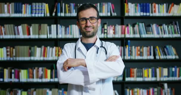 Médico Joven Hermoso Una Biblioteca Sonriendo Feliz Sosteniendo Libros Después — Vídeos de Stock