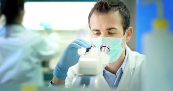 漂亮的年轻科学家男医生分析液体病毒细胞在专业实验室使用合格的设备和戴上眼镜以保护眼睛和照顾的实验室眼镜 — 图库视频影像