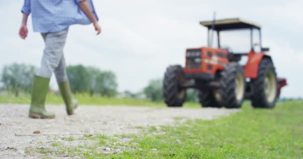 农民男子在农村领域走在橡胶靴拖拉机的视频 — 图库视频影像