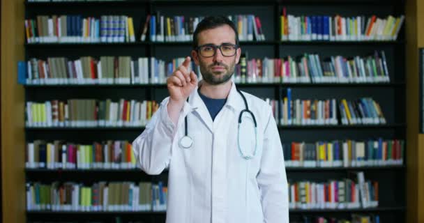 Jeune Beau Médecin Dans Une Bibliothèque Souriant Heureux Tenant Des — Video