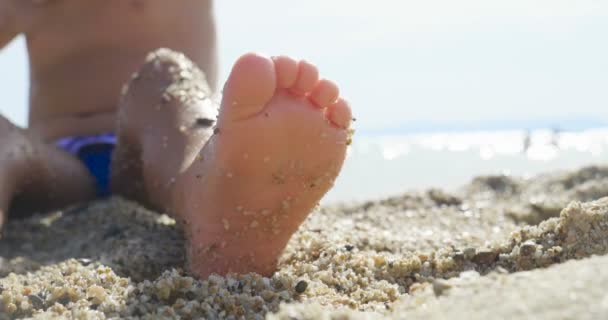 一个小女孩在海上的沙滩上玩耍 小腿和手指 穿着泳衣 背景是海黄沙和蓝水 — 图库视频影像