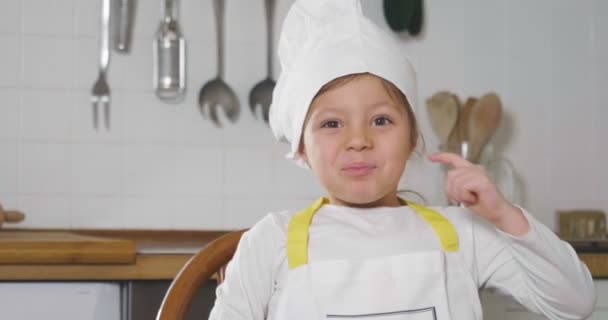 厨房里一个小女孩的肖像 打扮成一个专业的厨师 用她的手做确定 作为适当营养和正宗食物的标志 烹饪学校 — 图库视频影像