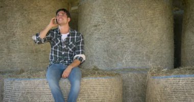 Yakışıklı genç bir çiftçi (öğrenci), bir gömlek bir mesaj, selfie, yazma Evet bir haystack üzerinde oturuyor mutlu gülümseyerek. Konsept: iletişim, ekoloji, tarım, saman, kişiler.