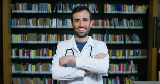 Médico Joven Hermoso Una Biblioteca Sonriendo Feliz Sosteniendo Libros Después — Vídeos de Stock