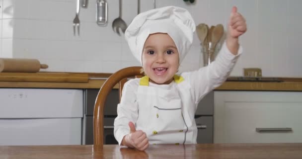 適切な栄養と本物食品の印として彼女の手で を作るプロ料理人として服を着て台所にある小さな女の子の肖像画 料理教室 — ストック動画